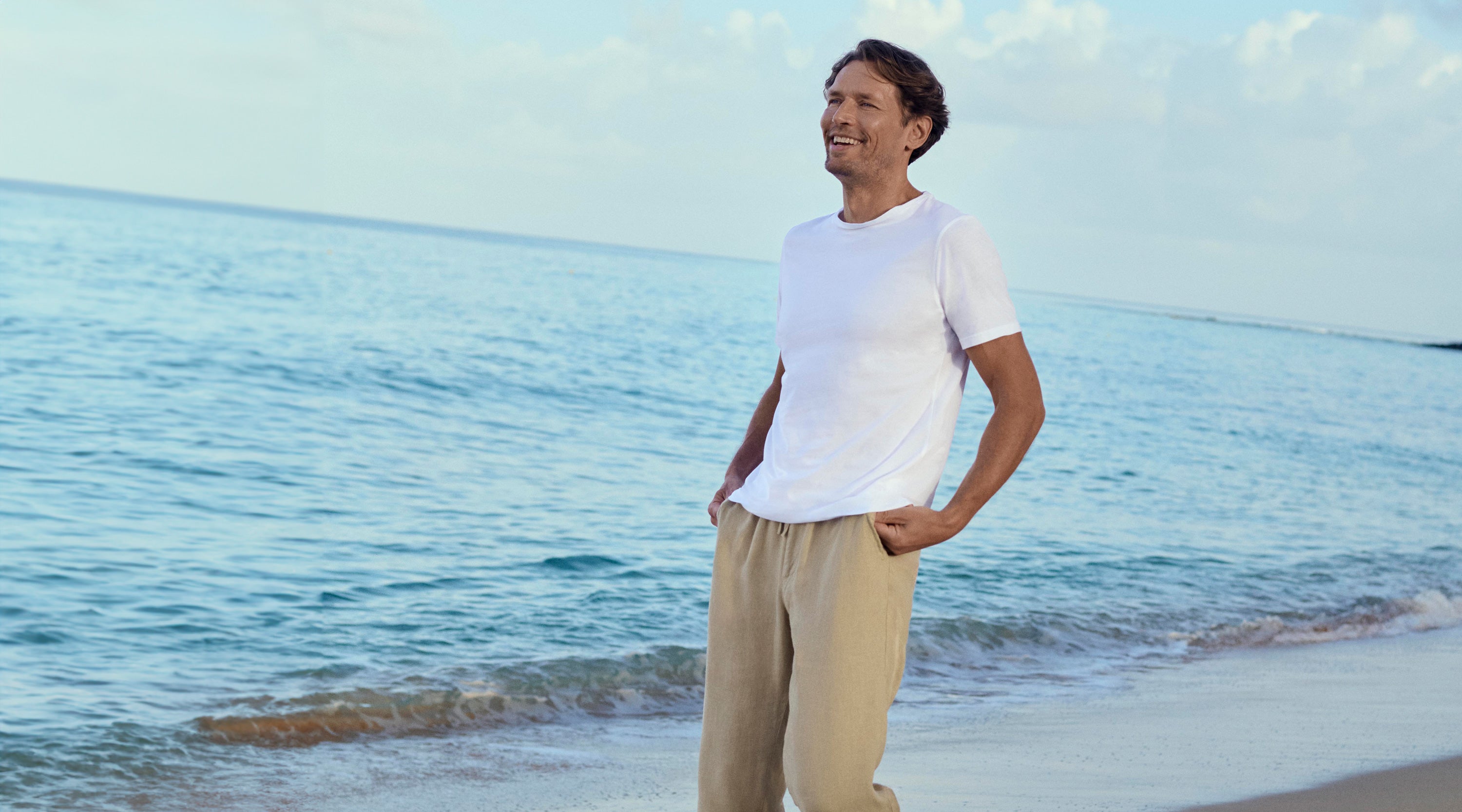 Man standing on a beach with ocean and sky in the background wearing mens linen trousers