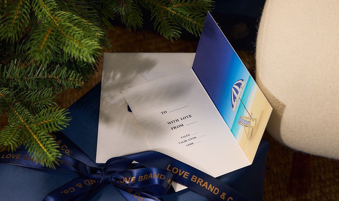 Gift box with a card and a card with a logo, surrounded by Christmas tree branches.