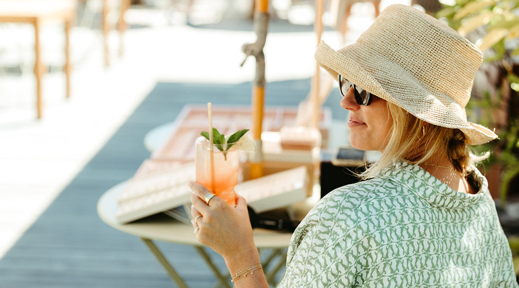 Woman in a sun hat and sunglasses holding a drink outdoors