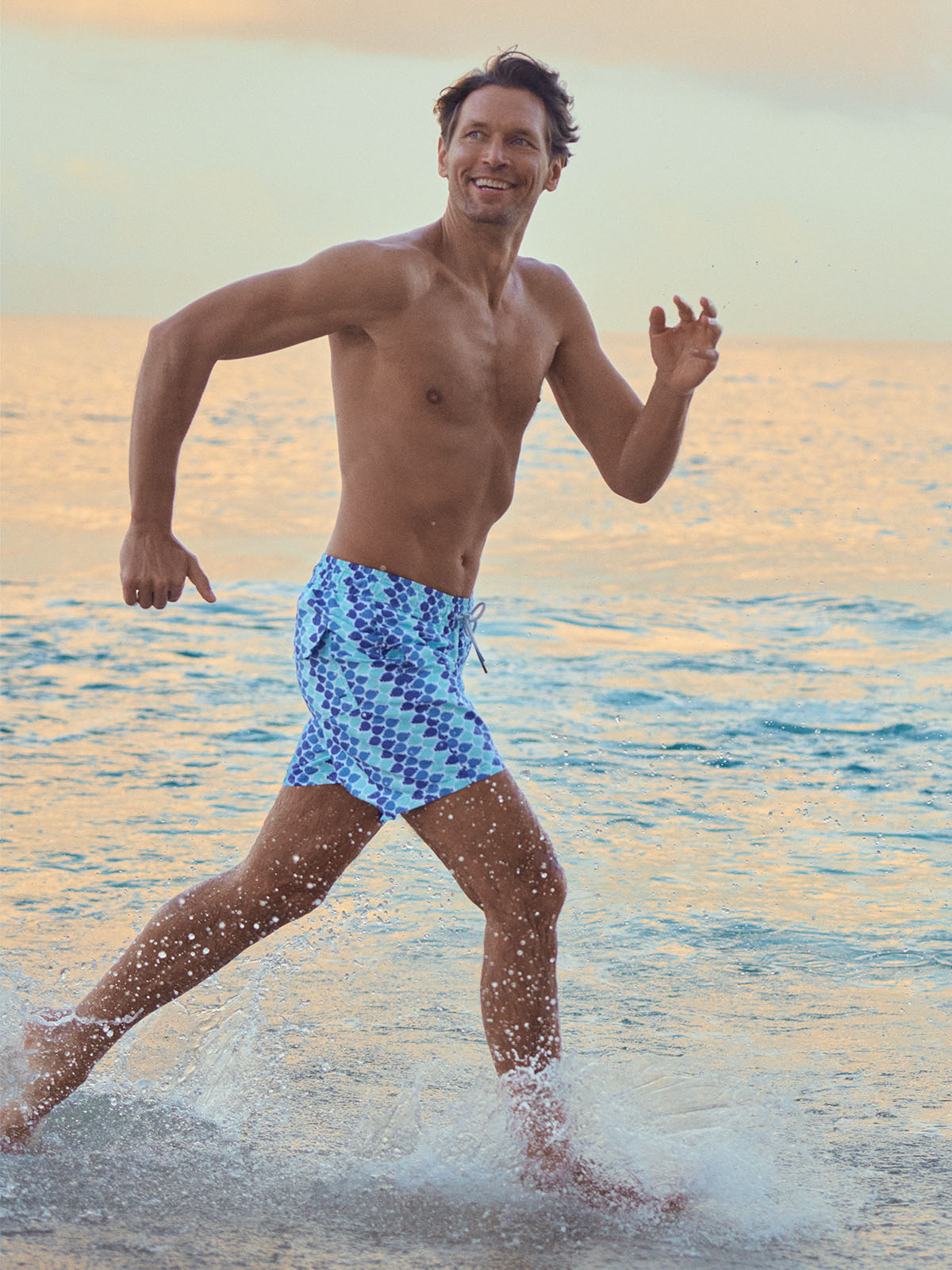 man running through sea wearing blue swim shorts