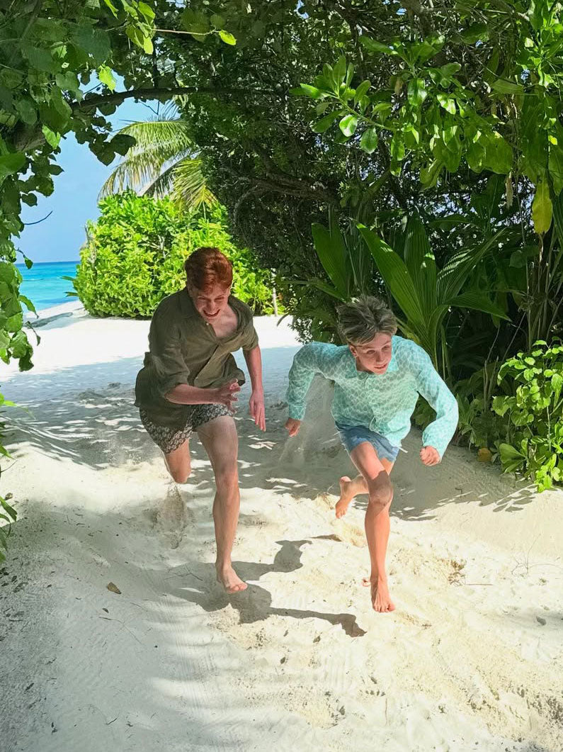 Two boys run across a sandy beach wearing linen clothing by luxury beachwear brand love brand & co.