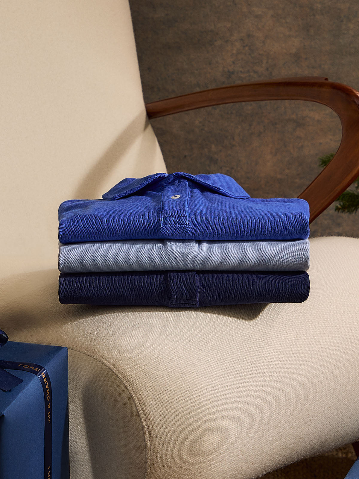 3 blue folded mens polo shirts on a chair
