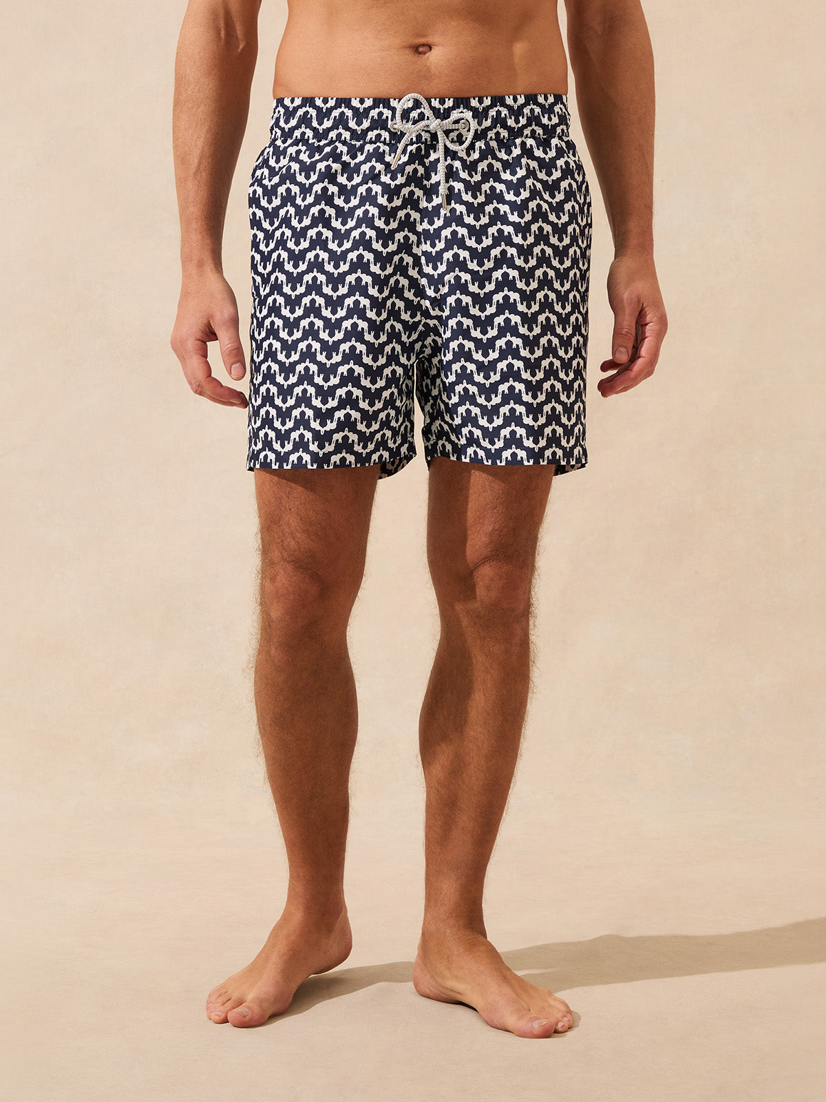 Man wearing navy and white patterned swim shorts on a beige background