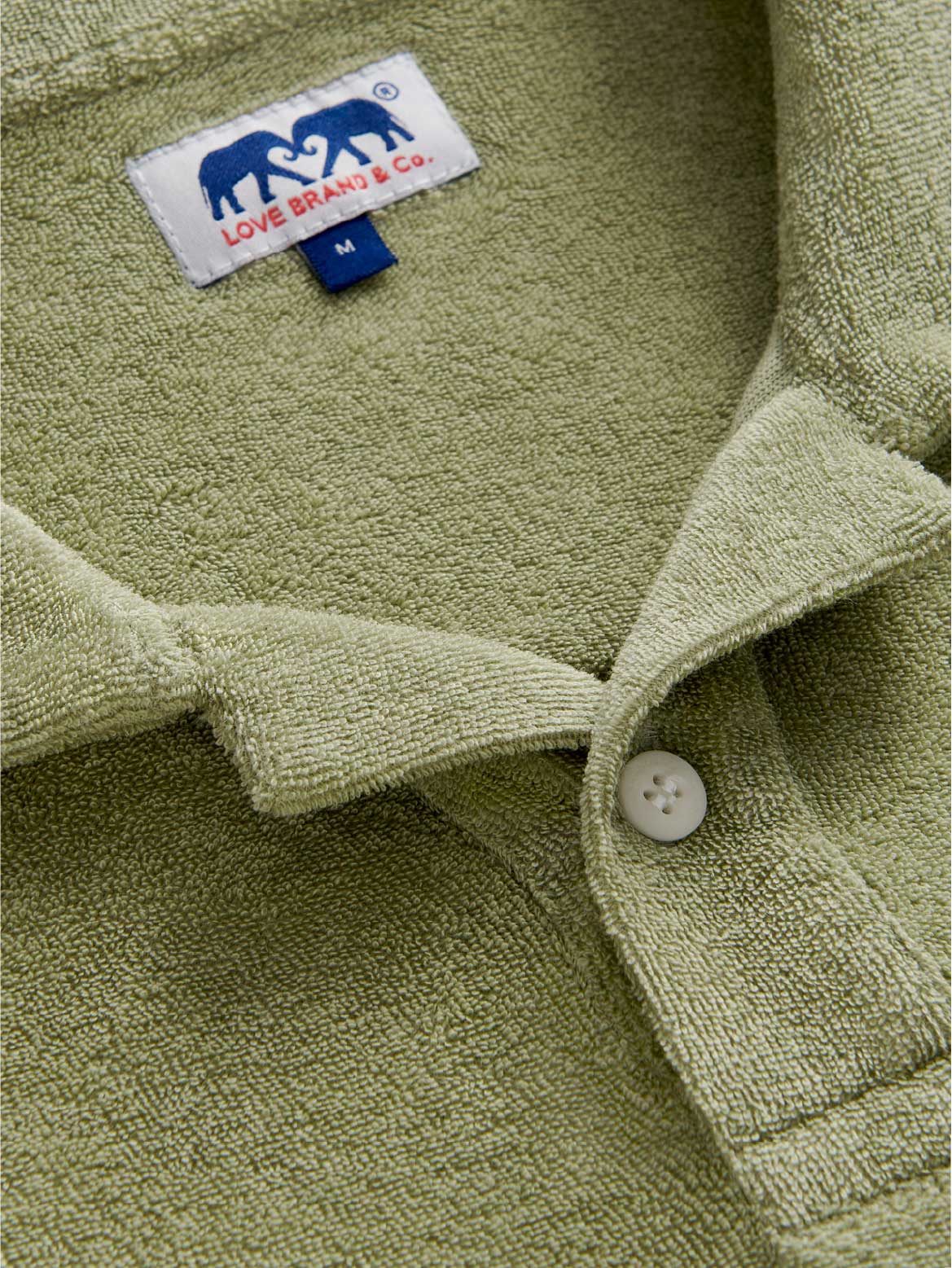 Close-up view of the collar of love brand green terry polo shirt showing love brand elephant label.