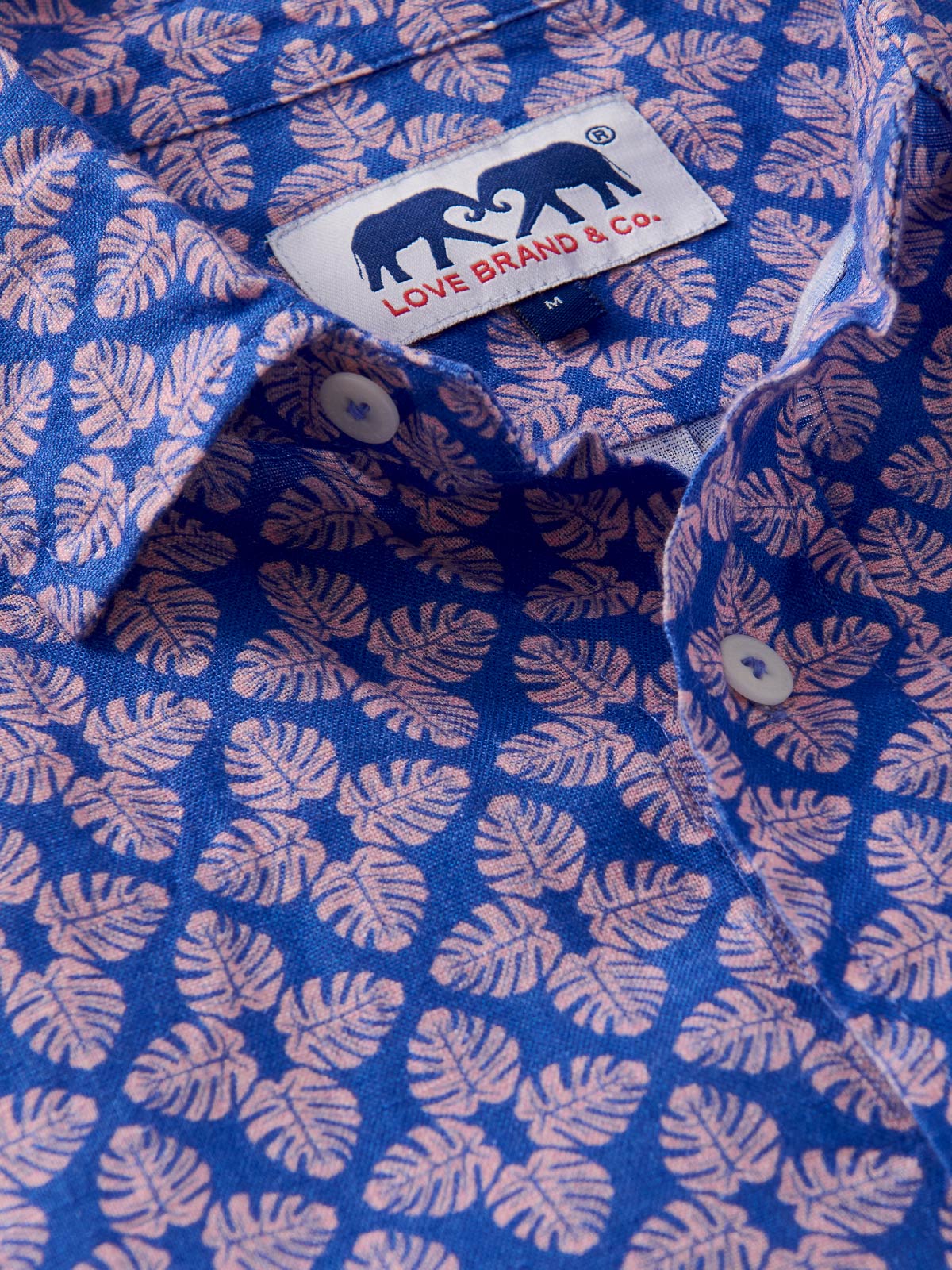 Close-up of a blue linen shirt with pink leaf pattern and Love Brand & Co. label.