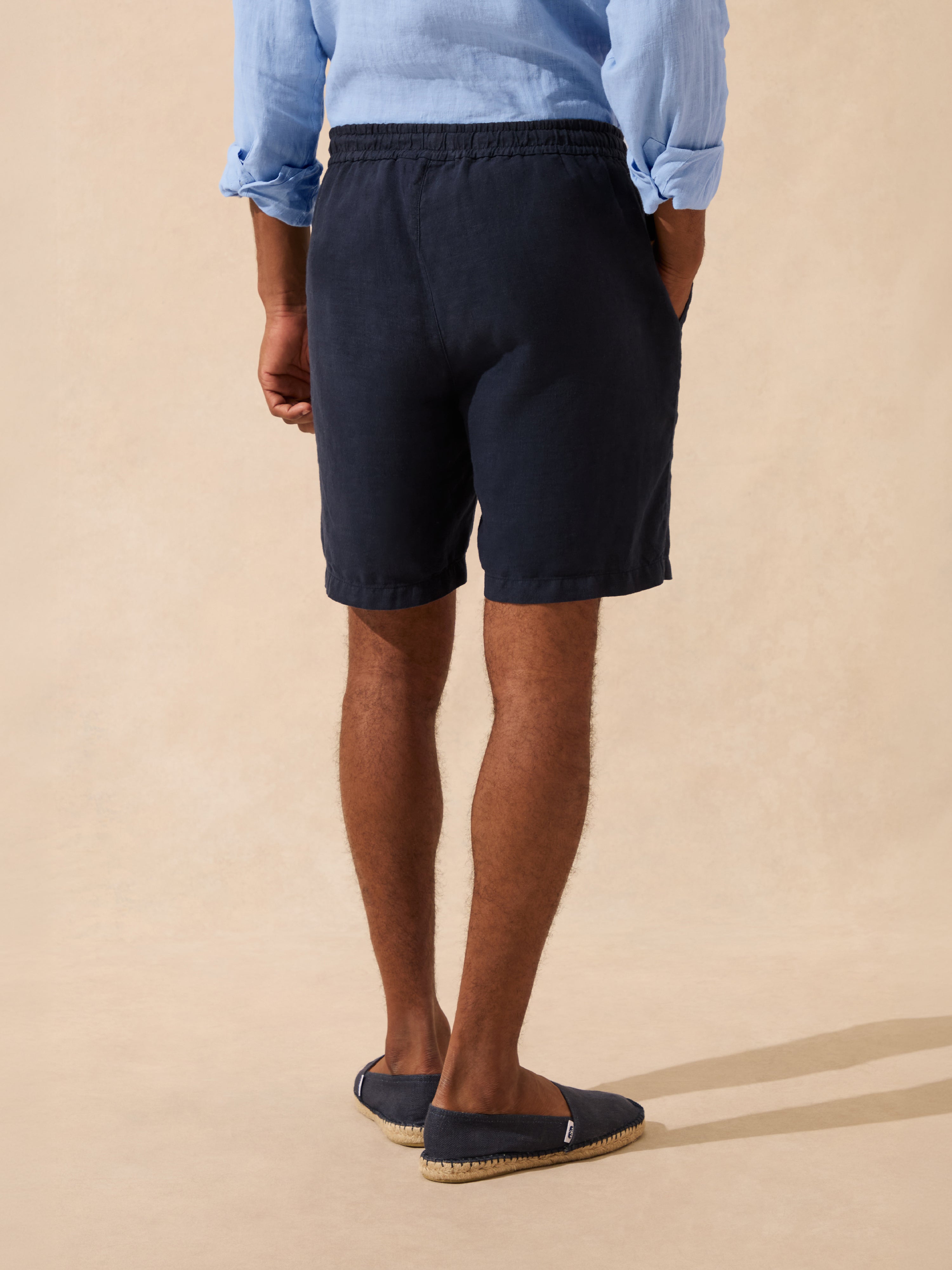 Person wearing navy shorts and a light blue shirt on a beige background