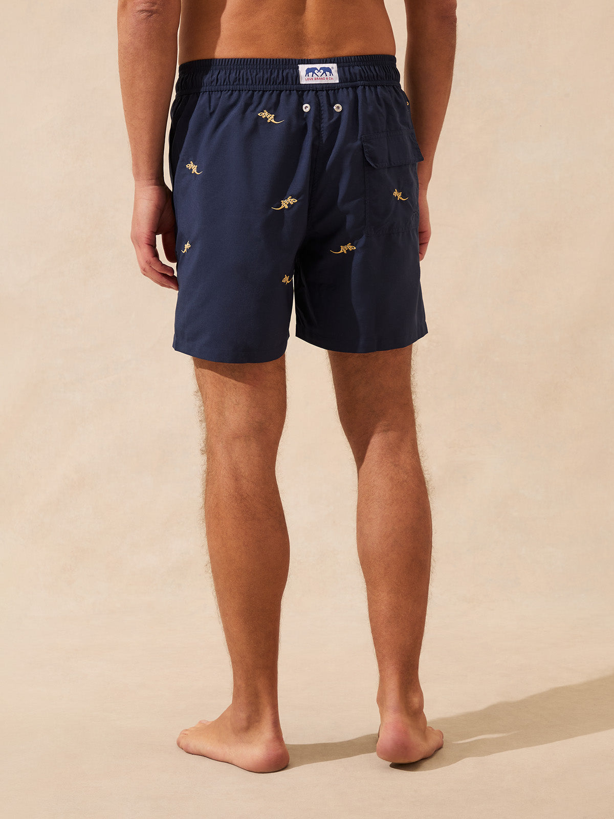 Man wearing navy swim shorts with embroidered geckos and a back pocket