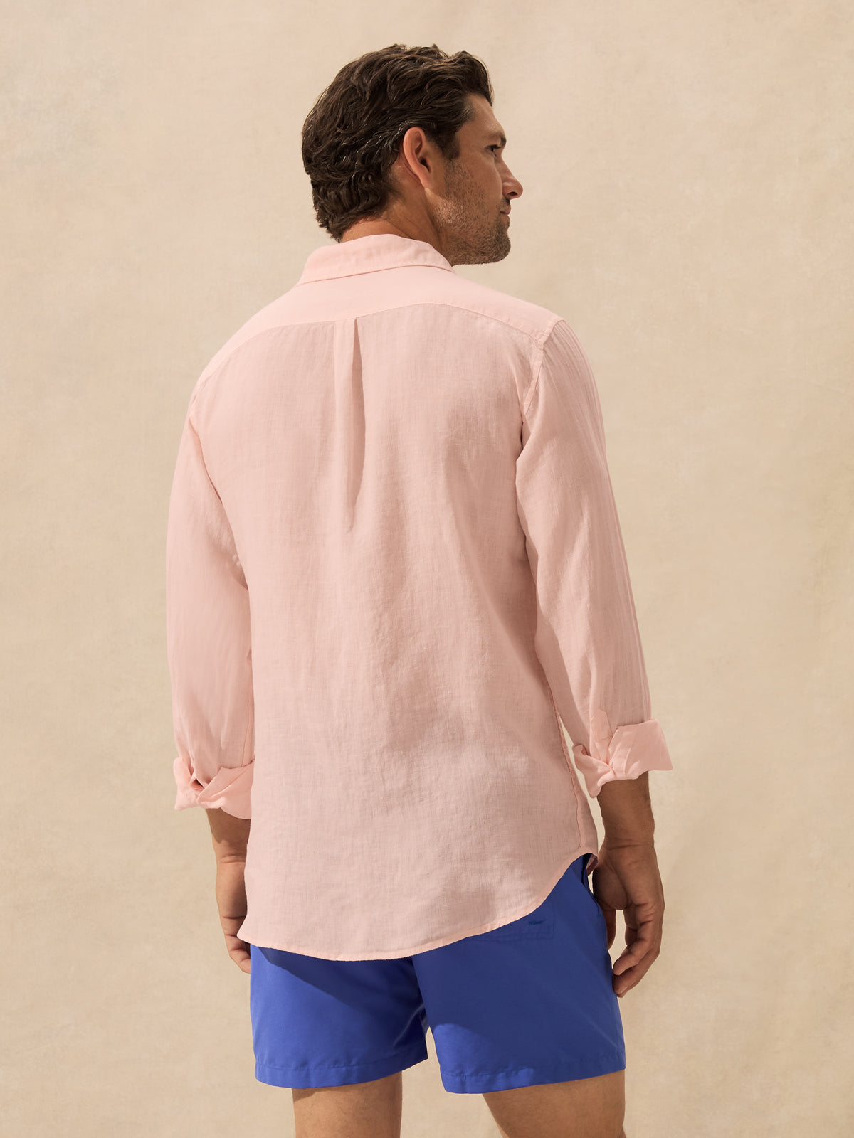 A man shown from the back wearing a light pink linen button-down shirt with rolled-up sleeves.