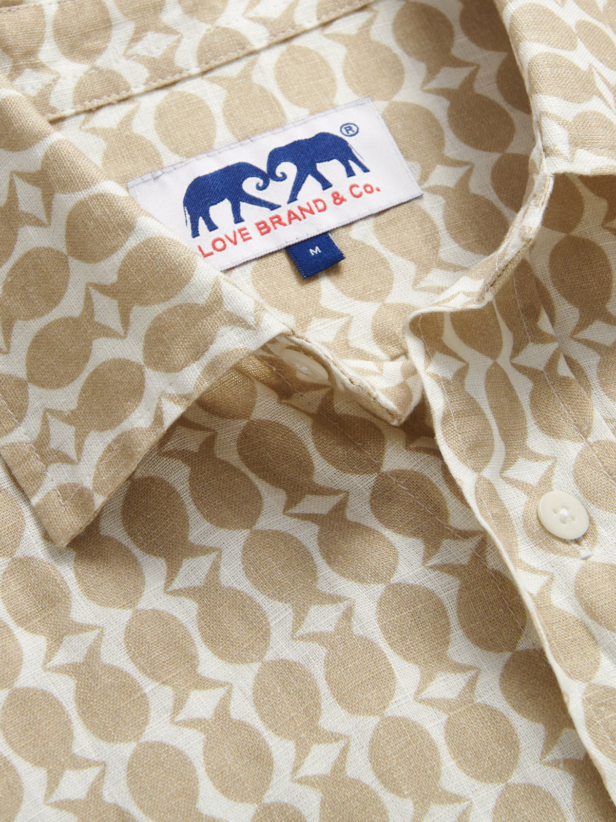Close-up view of Men's Pina Colada Abaco Linen Shirt collar. Showcasing love brand logo and brown and white pineapple and fish pattern.