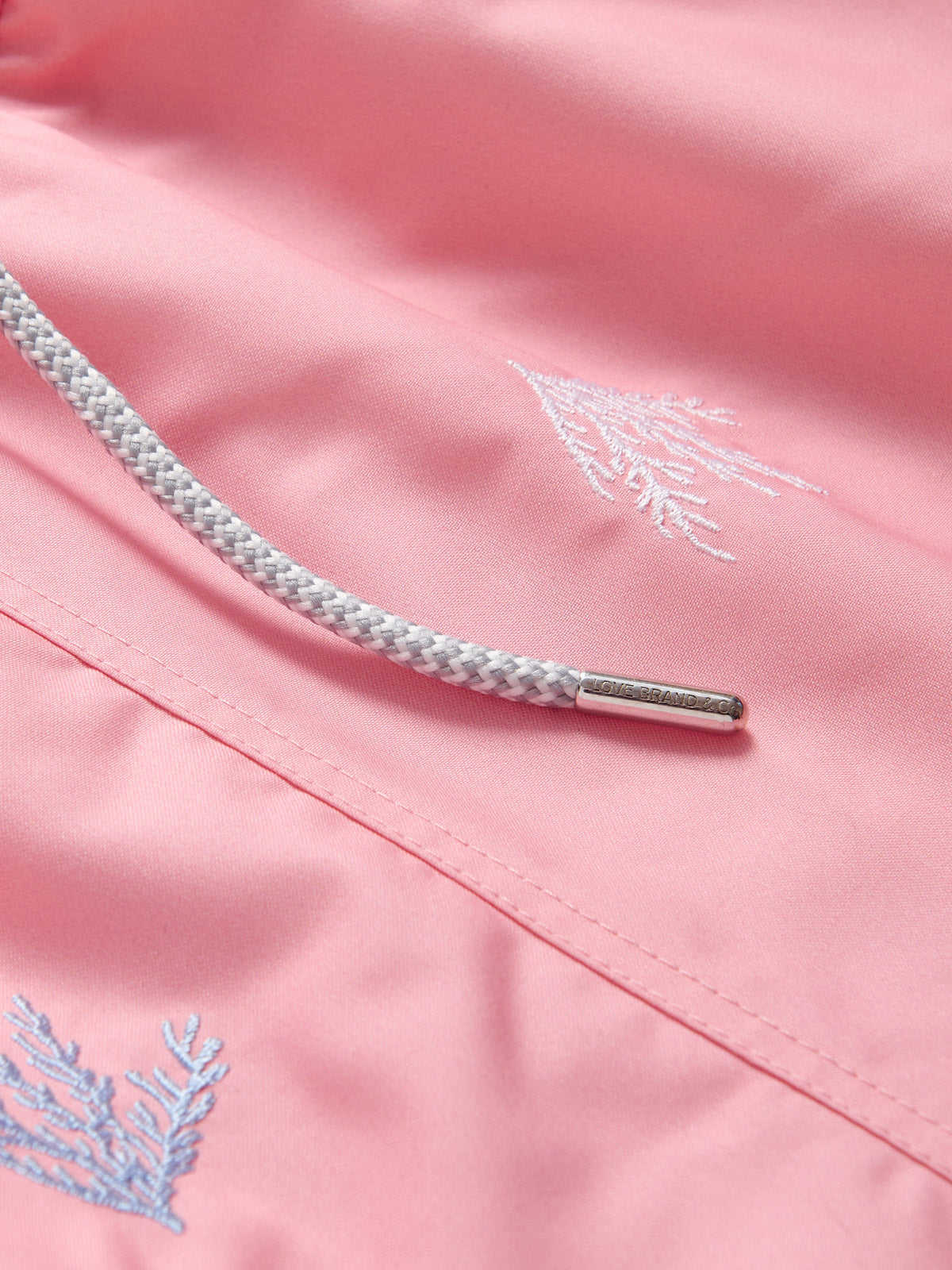 Close-up of a pink fabric with embroidered designs and a metal drawstring.