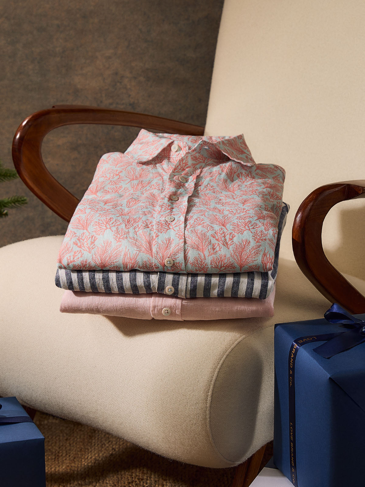 Stack of folded linen shirts on a chair next to a blue gift box