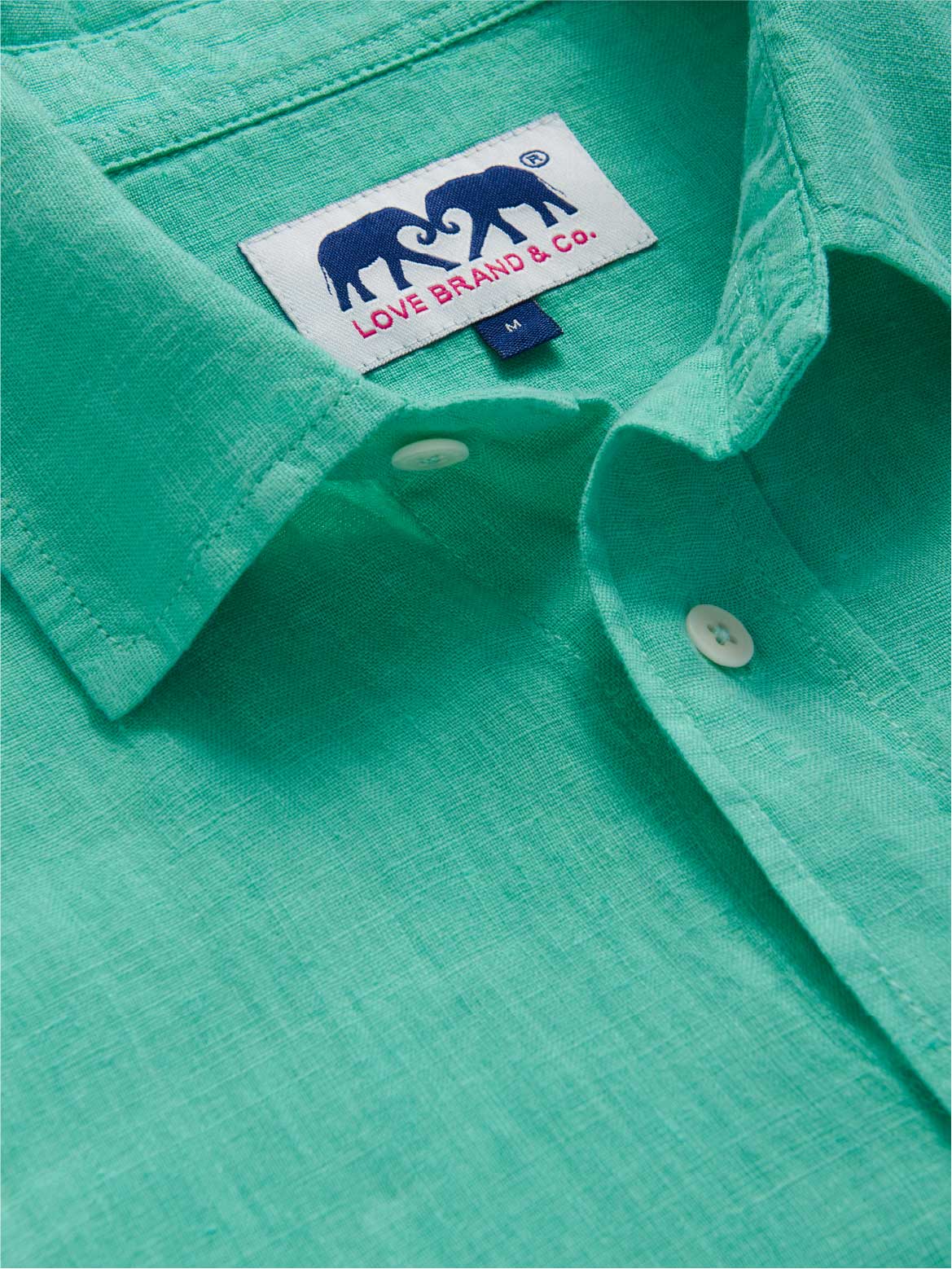 Close-up of a teal shirt with a love brand label featuring two elephants and text.