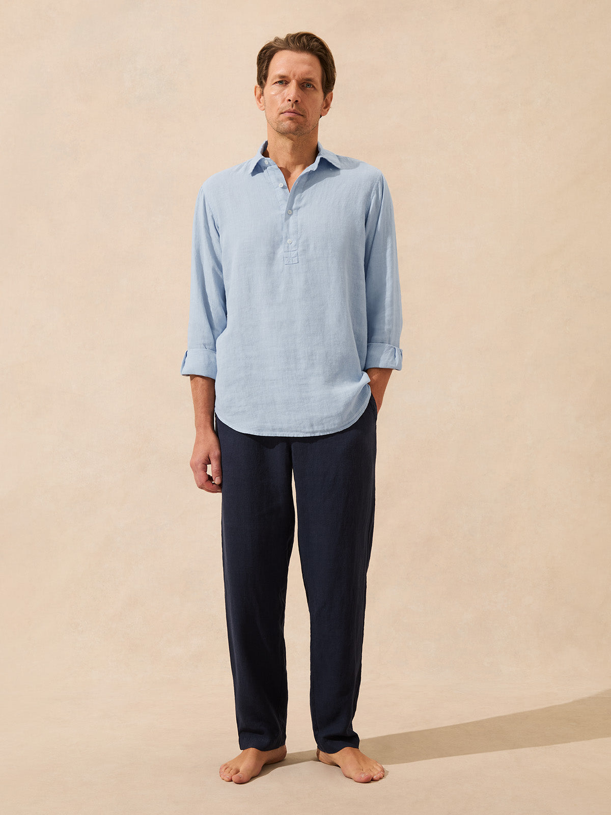Man wearing a light blue shirt and dark pants against a beige background