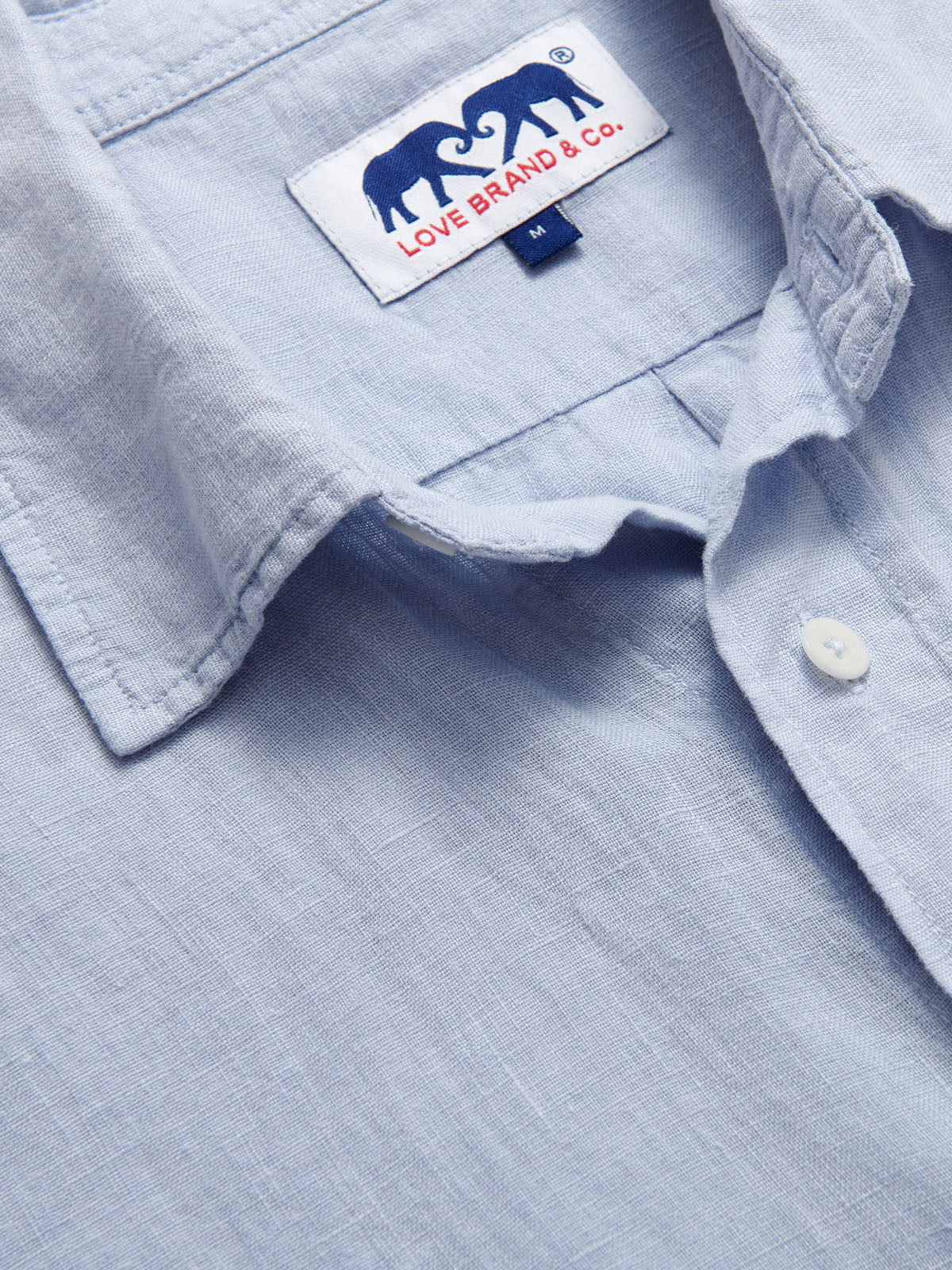 Close-up of Men's Sky Blue Manjack Linen Shirt. Men's linen shirt close-up image showcasing the soft fabric texture and brand label.
