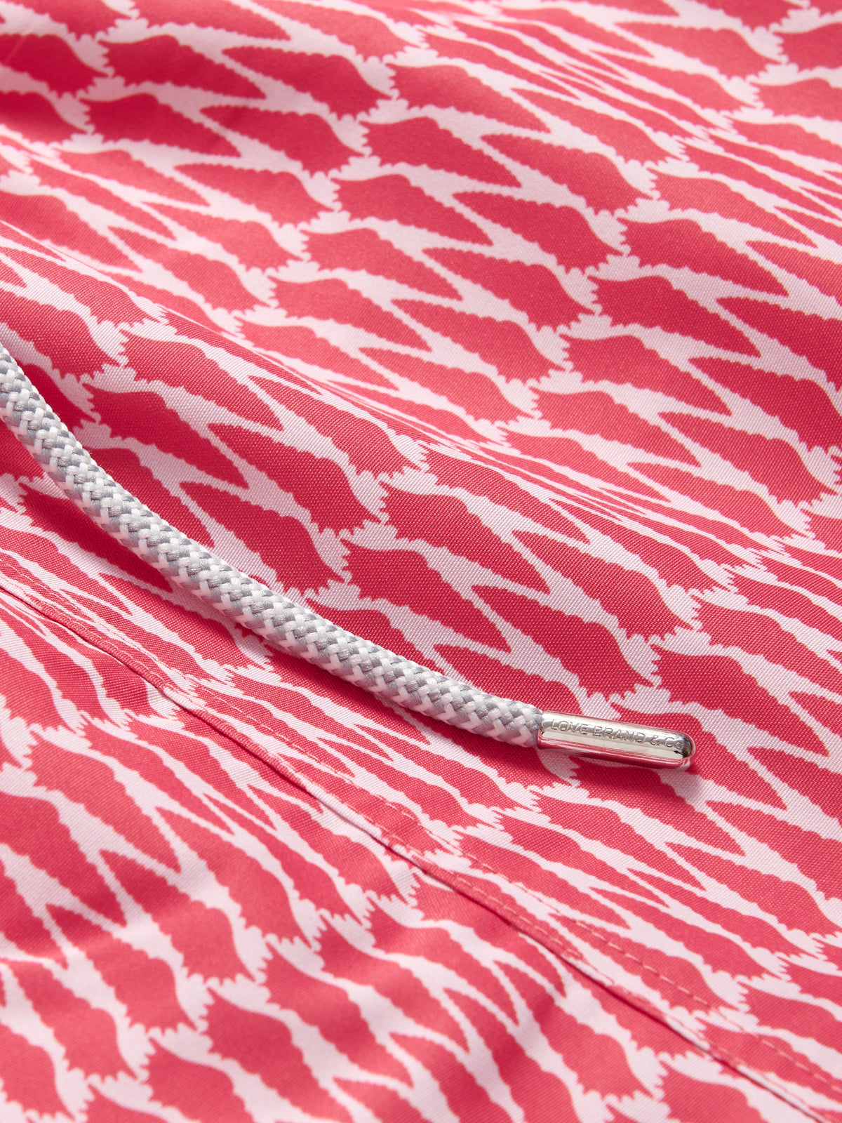 Close-up view of red swimming shorts men showing white and red conch shell print.