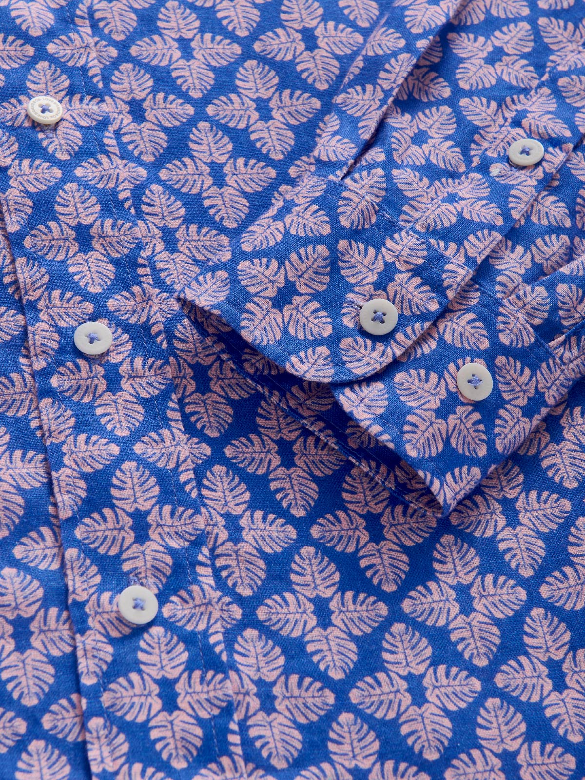 Close-up of a blue shirt with pink leaf pattern showing cuff details.