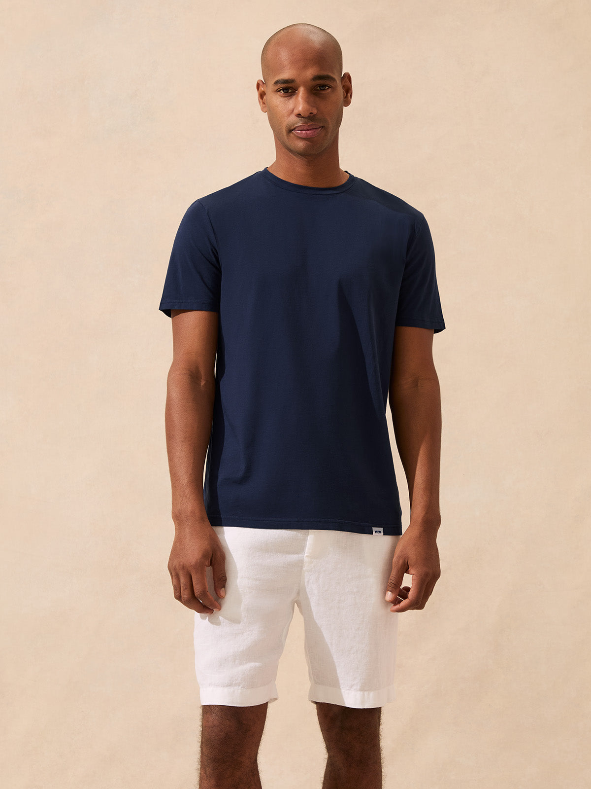 Man wearing a navy t-shirt and white shorts against a beige background