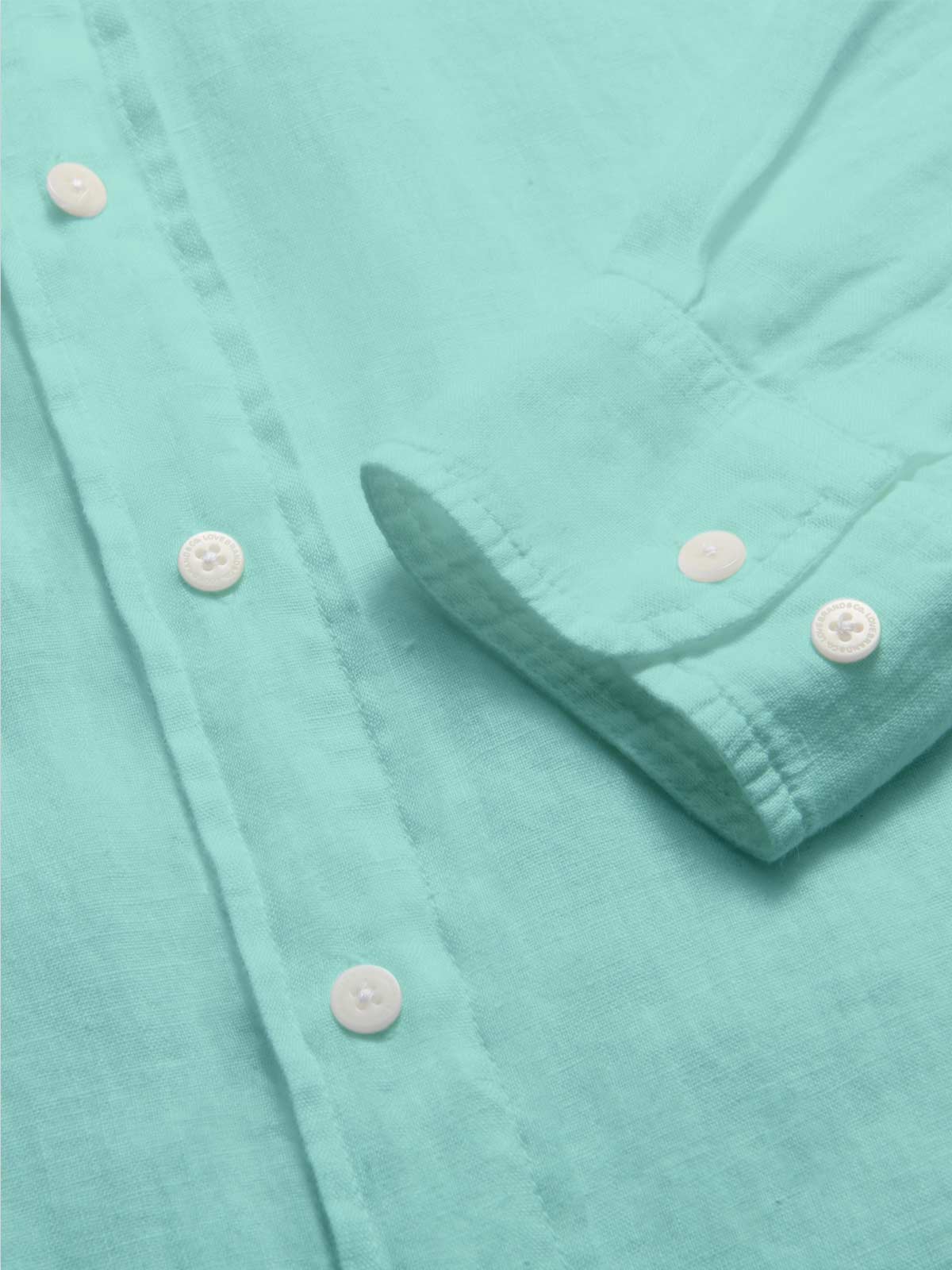 Close-up view of the Men's Cay Green Abaco Linen Shirt fabric, showcasing the vibrant green hue and fine texture of the 100% linen material.