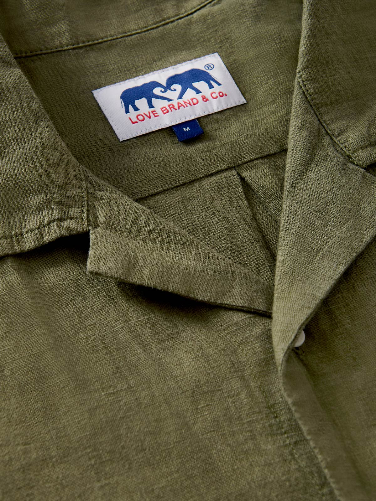 Close-up of a green linen shirt with a love brand label featuring two elephants.