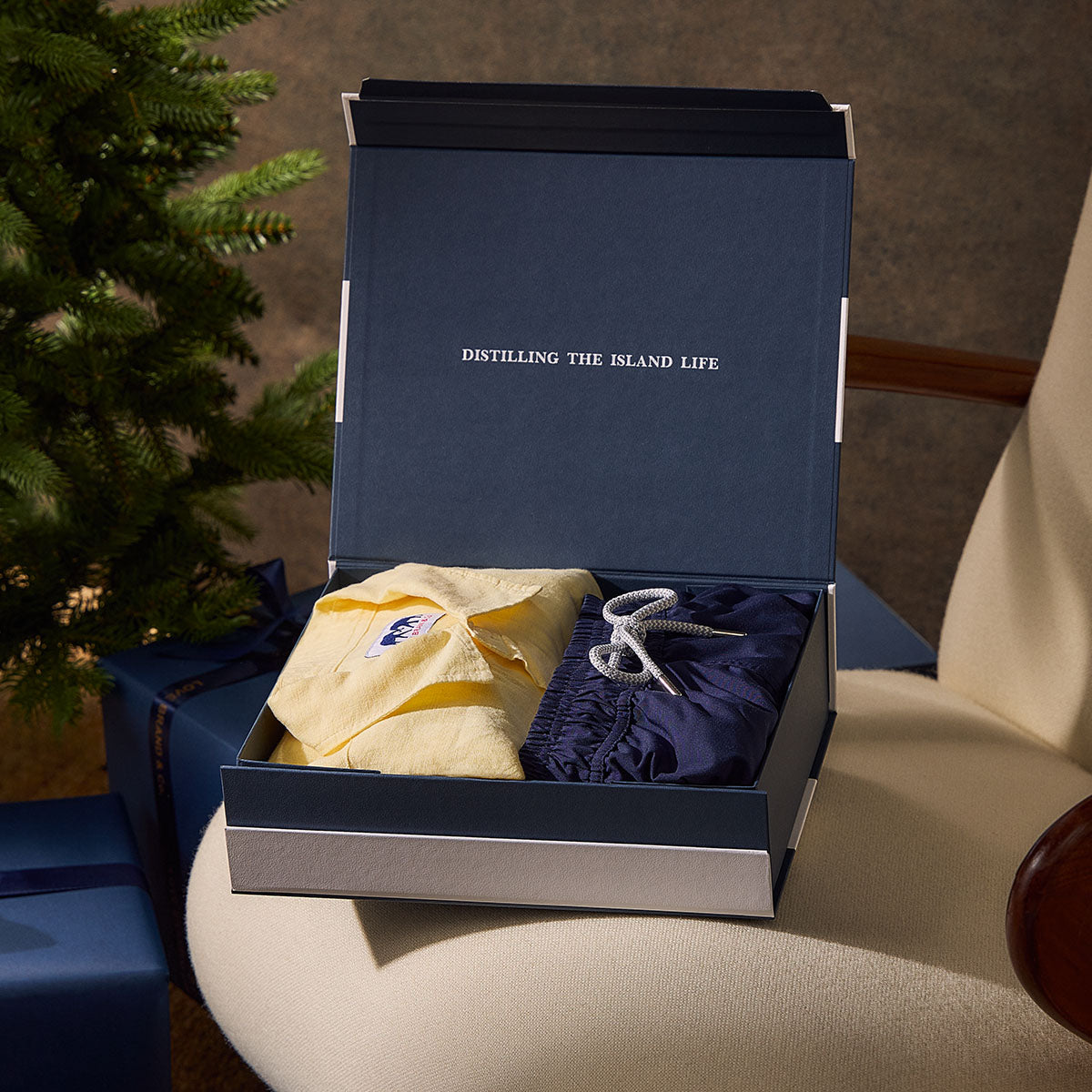 Open navy blue gift box with yellow linen shirt and navy blue swim shorts.