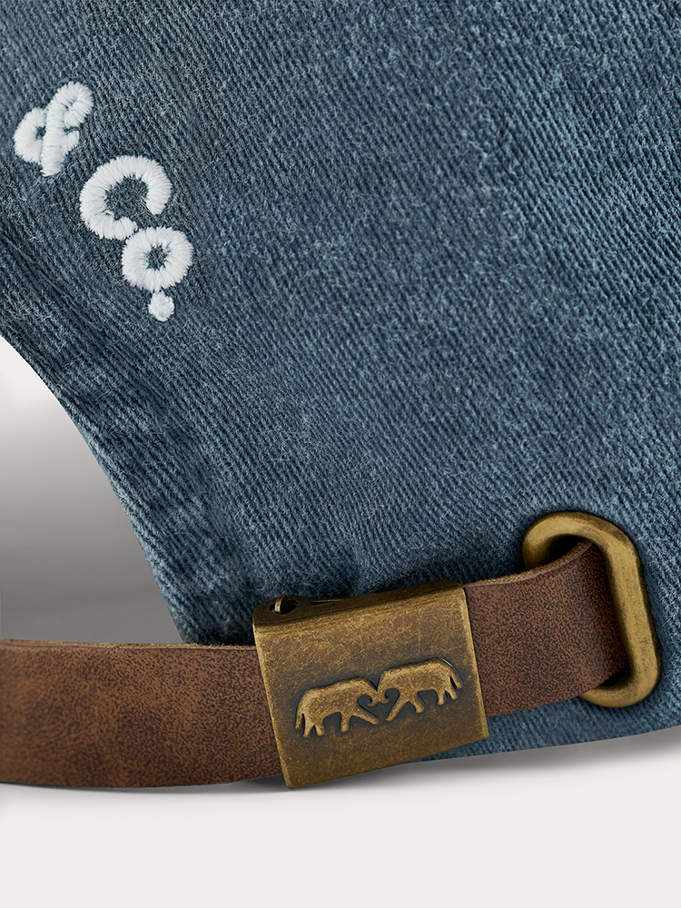 Close-up of a blue denim product with a brown leather belt and brass buckle, featuring a brand logo.