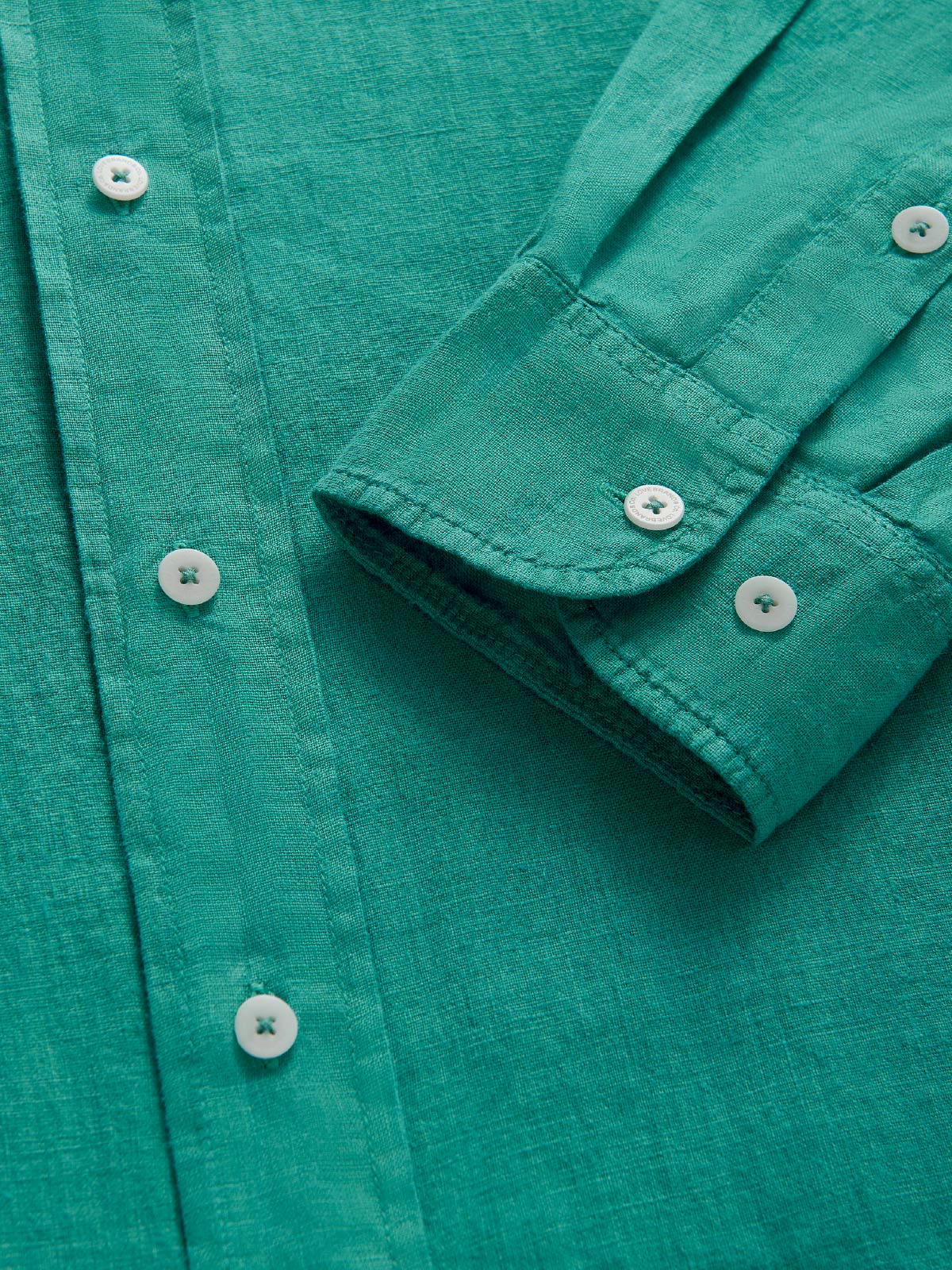 Close-up of a teal shirt with buttons and long sleeves.