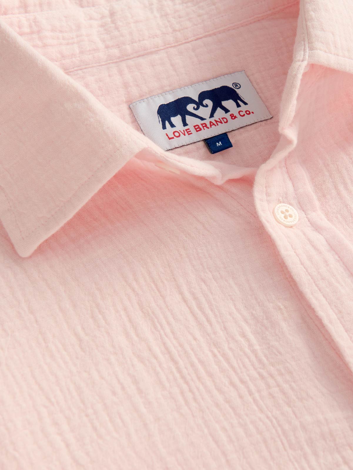 Close-up of a pink shirt crafted from 100% cotton with a brand label featuring elephants.