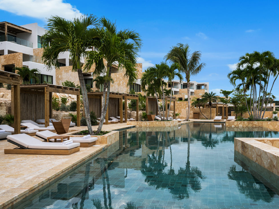 Pool area at The Strand with lounge chairs, palm trees, and a building in the background under a clear blue sky.