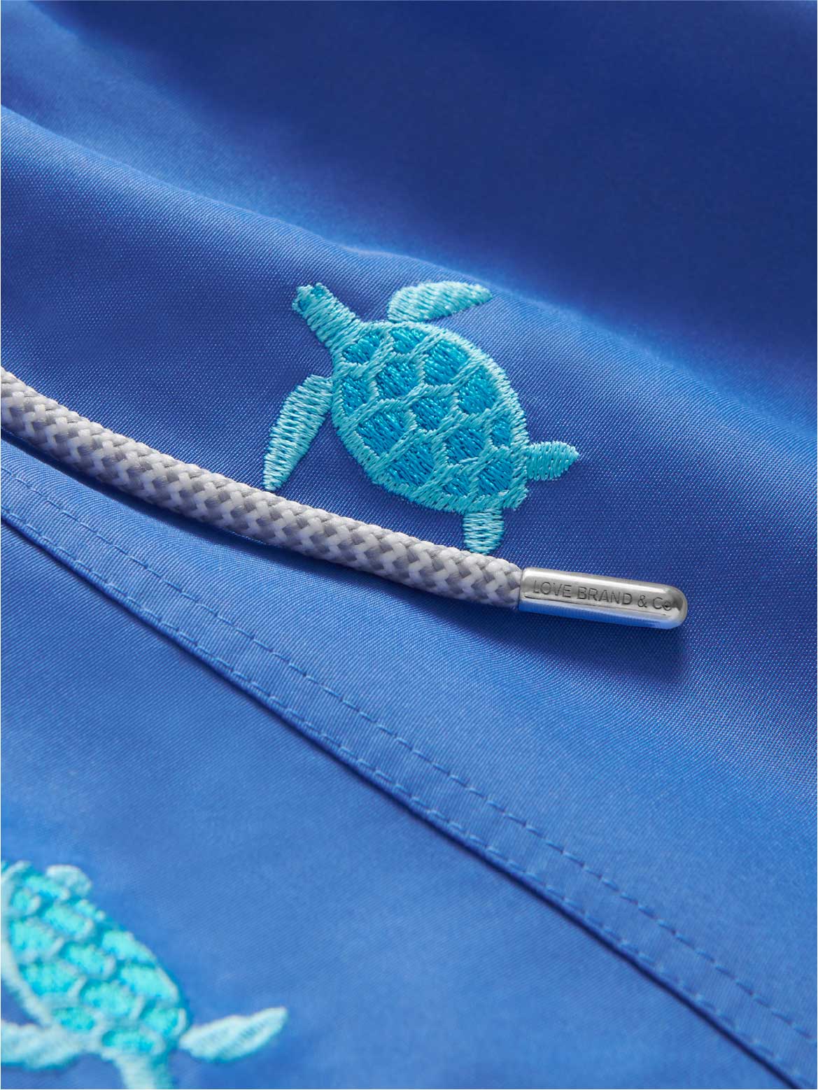 Close-up view of mens turtles hold on swim shorts. Embroidered blue turtles on a blue swim short fabric.
