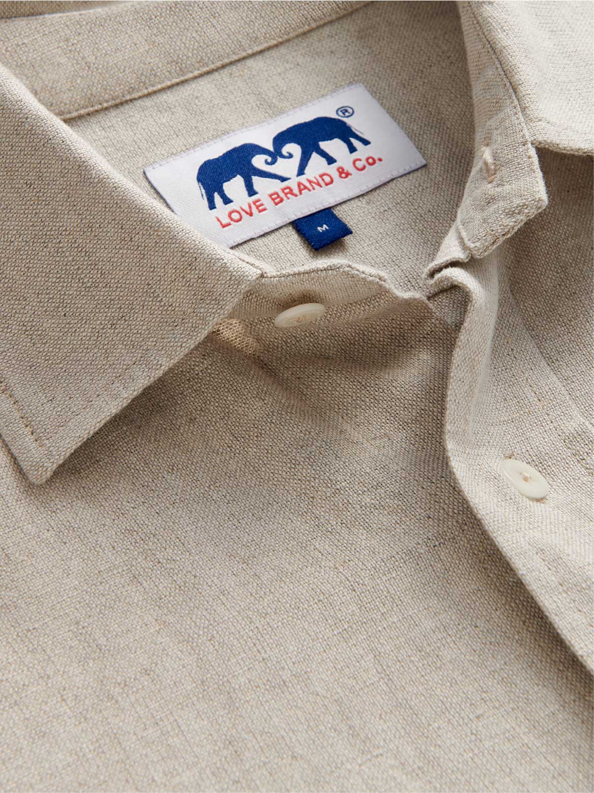 Close-up of a beige shirt with a visible love brand label featuring two elephants and text.