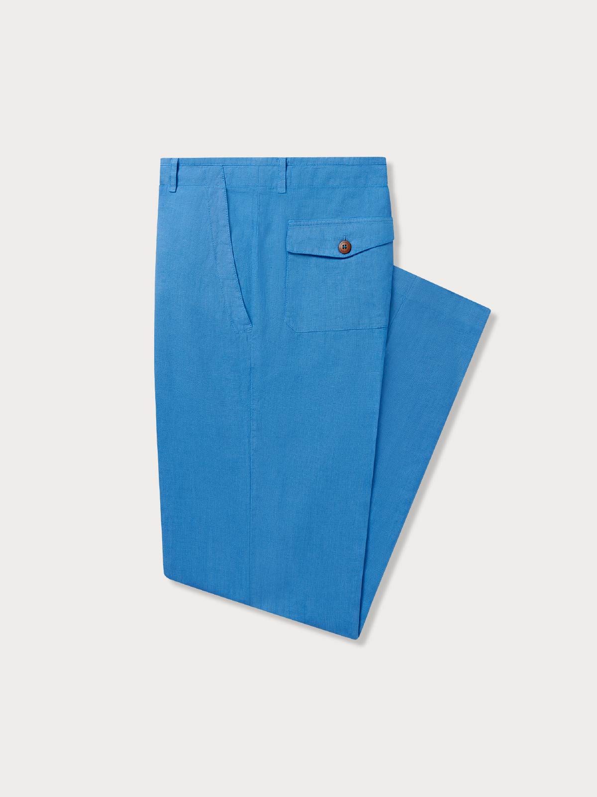 Side view of a pair of folded blue linen trousers showing back button pocket on a grey background.