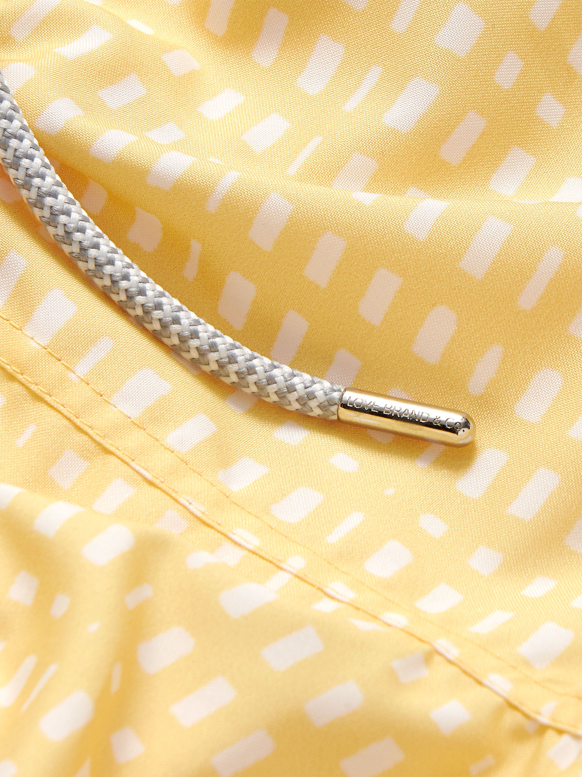 Close-up of Boys Deck Chairs Staniel Swim Shorts fabric in yellow with white patterns and a grey drawstring.