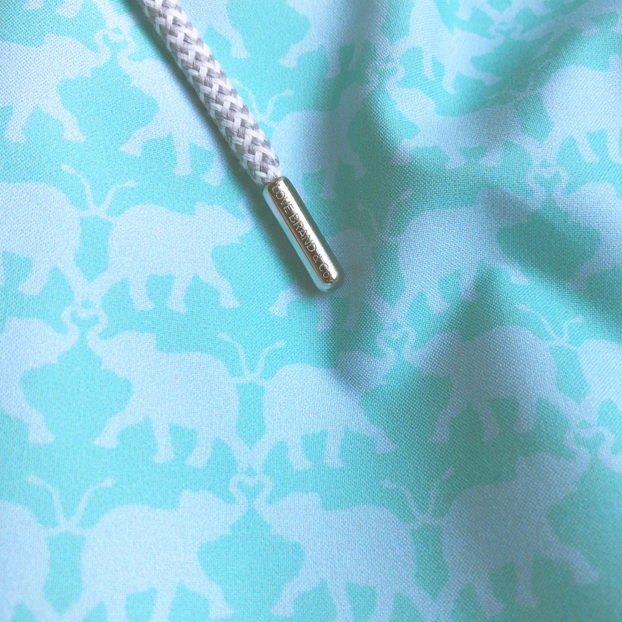 close-up view of mint swim shorts with an elephant print and drawstring