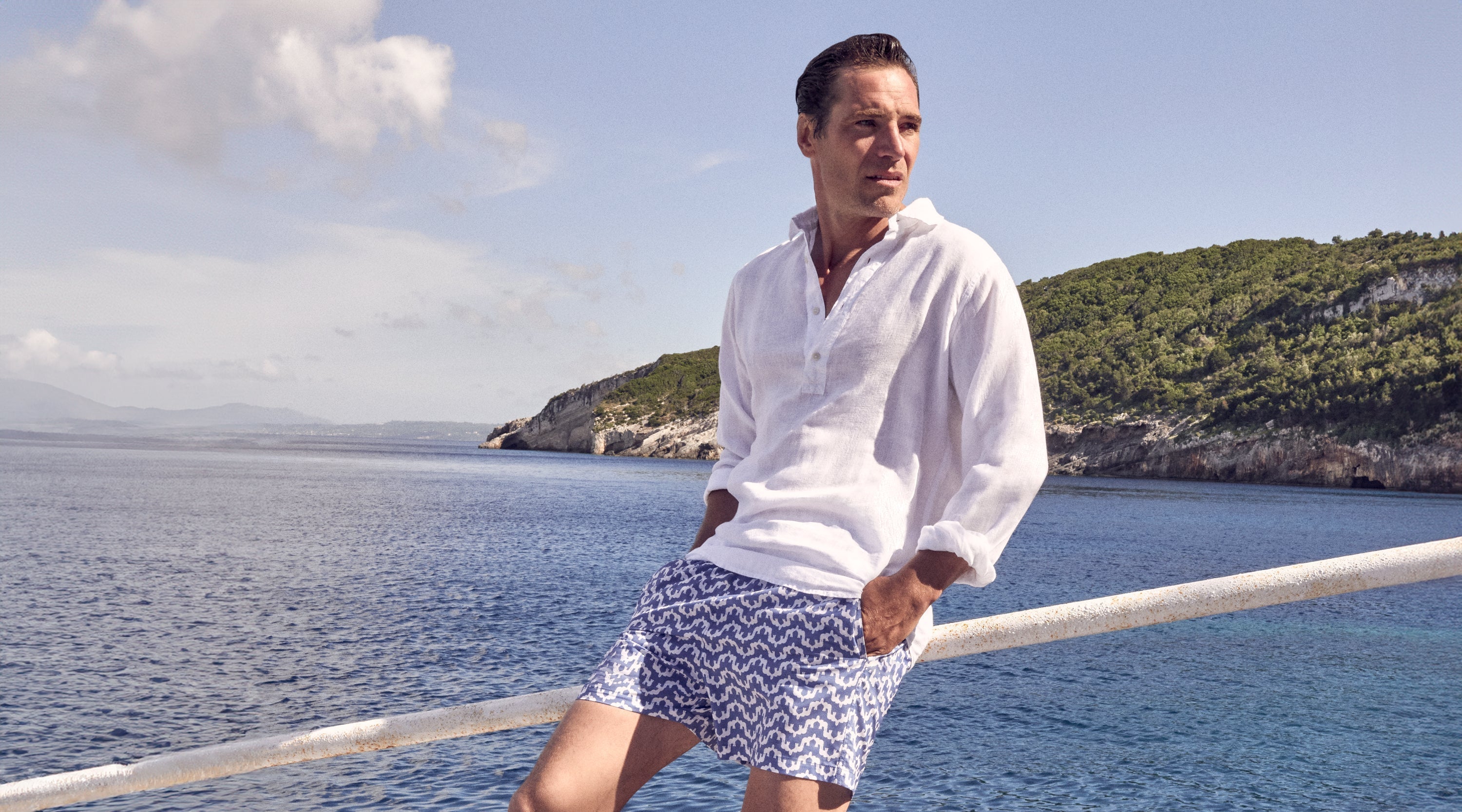 Man wears blue swim shorts and white linen shirt