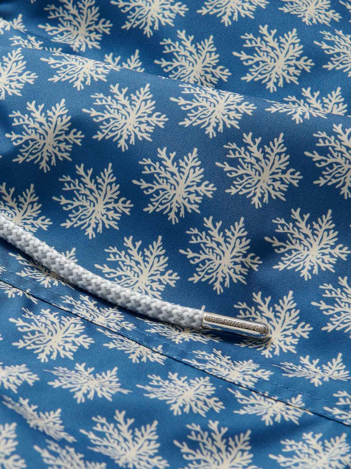 Men's Coral Clusters Staniel Swim Shorts featuring intricate coral patterns in stone shades on a blue background. Patterned swim shorts made of premium fabric and drawstring detail.