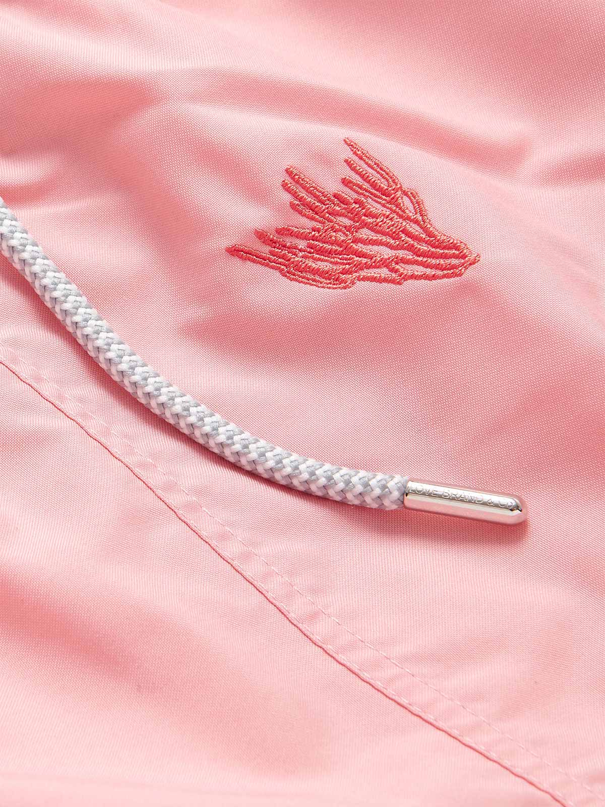 Close-up of pastel pink swim shorts featuring coral embroidery. Embroidered swim shorts with a braided drawstring with a metallic tip.