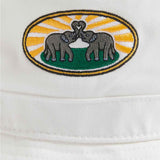 White cotton twill bucket hat with vibrant woven patch of two elephants with intertwined trunks, set against a background of sun rays and greenery.