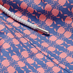 Close-up image of Men's Crab Pool Staniel Swim Shorts. Patterned swim shorts featuring a pattern of pink crabs on a deep blue base with a white drawstring.