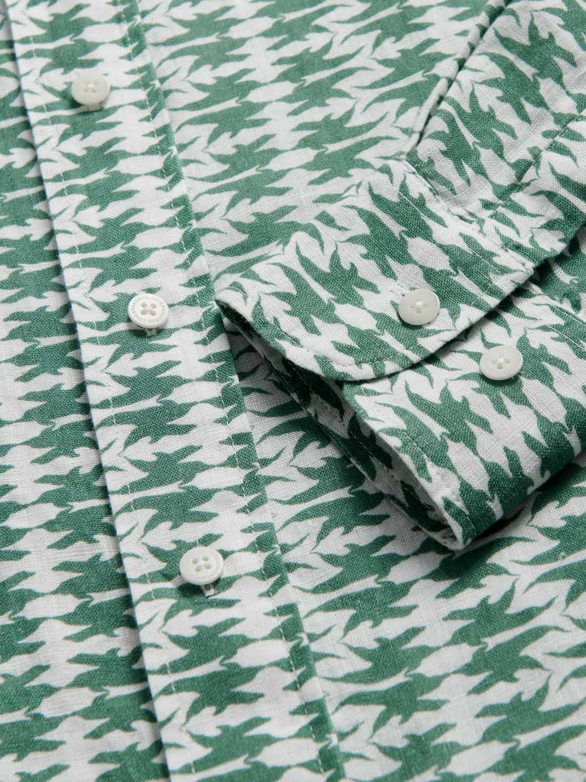 Close-up of the Men's Dolphins of Greece Abaco Linen Shirt, showcasing the green and white dolphin print, button-down front, and classic collar with signature engraved corozo nut buttons.