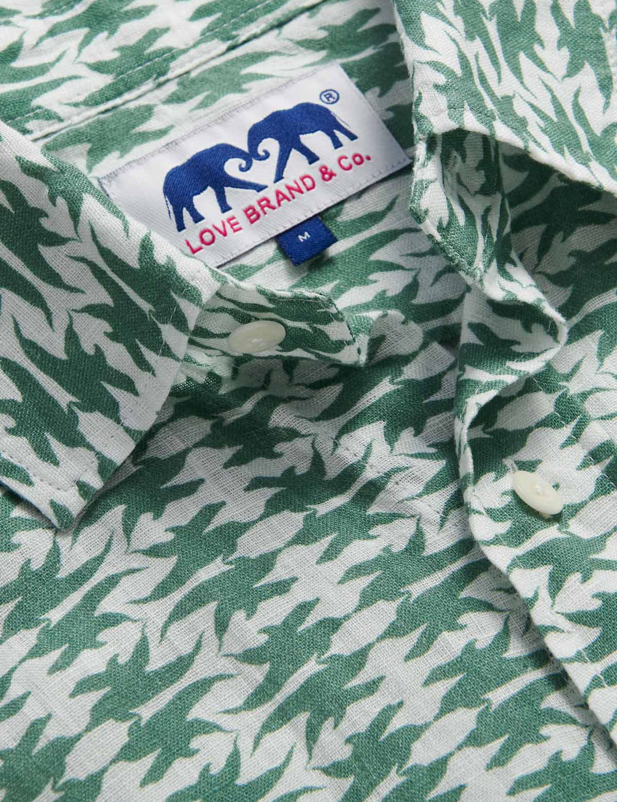 Close-up of the Men's Dolphins of Greece Abaco Linen Shirt showcasing the green and white dolphin print with a visible Love Brand & Co. label. Old money shirts made from 100% cotton.