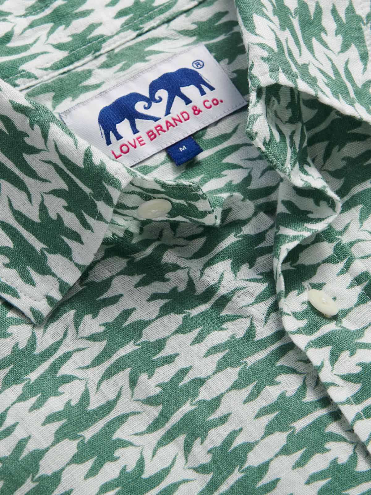 Close-up of the Men's Dolphins of Greece Abaco Linen Shirt showcasing the green and white dolphin print with a visible Love Brand & Co. label. Old money shirts made from 100% cotton.