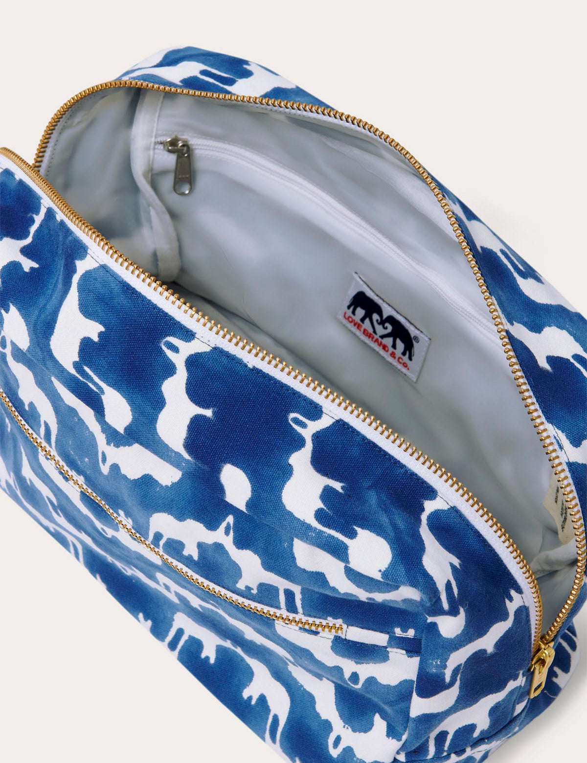 Canvas wash bag in blue featuring a block-printed pattern of Asian elephants forming the illusion of Indian palaces; shown with an open zipper displaying internal compartments and a recycled plastic lining.