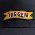 Navy blue trucker cap with "The G.E.M." logo label on the front.