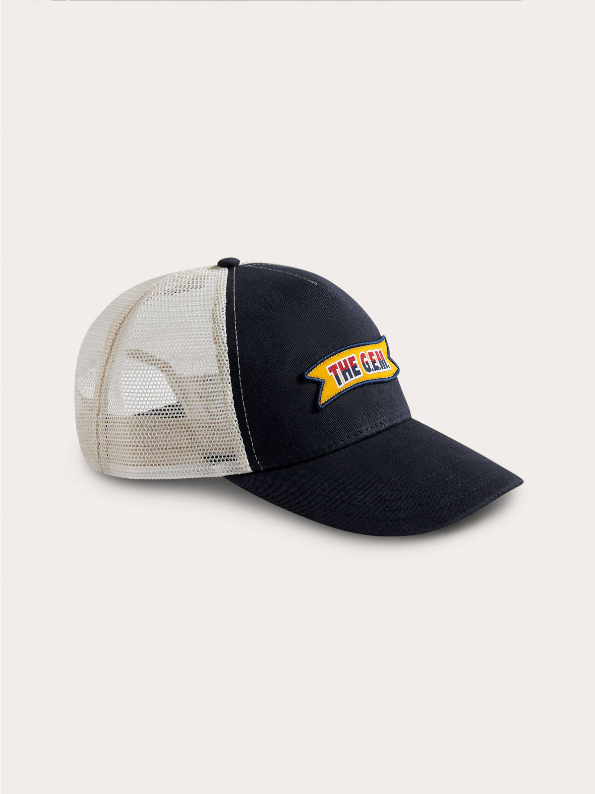 Adjustable navy and stone trucker cap featuring the G.E.M. Ribbon logo label with a merrowed edge on a navy cotton twill crown and visor, and contrast stone trucker mesh.