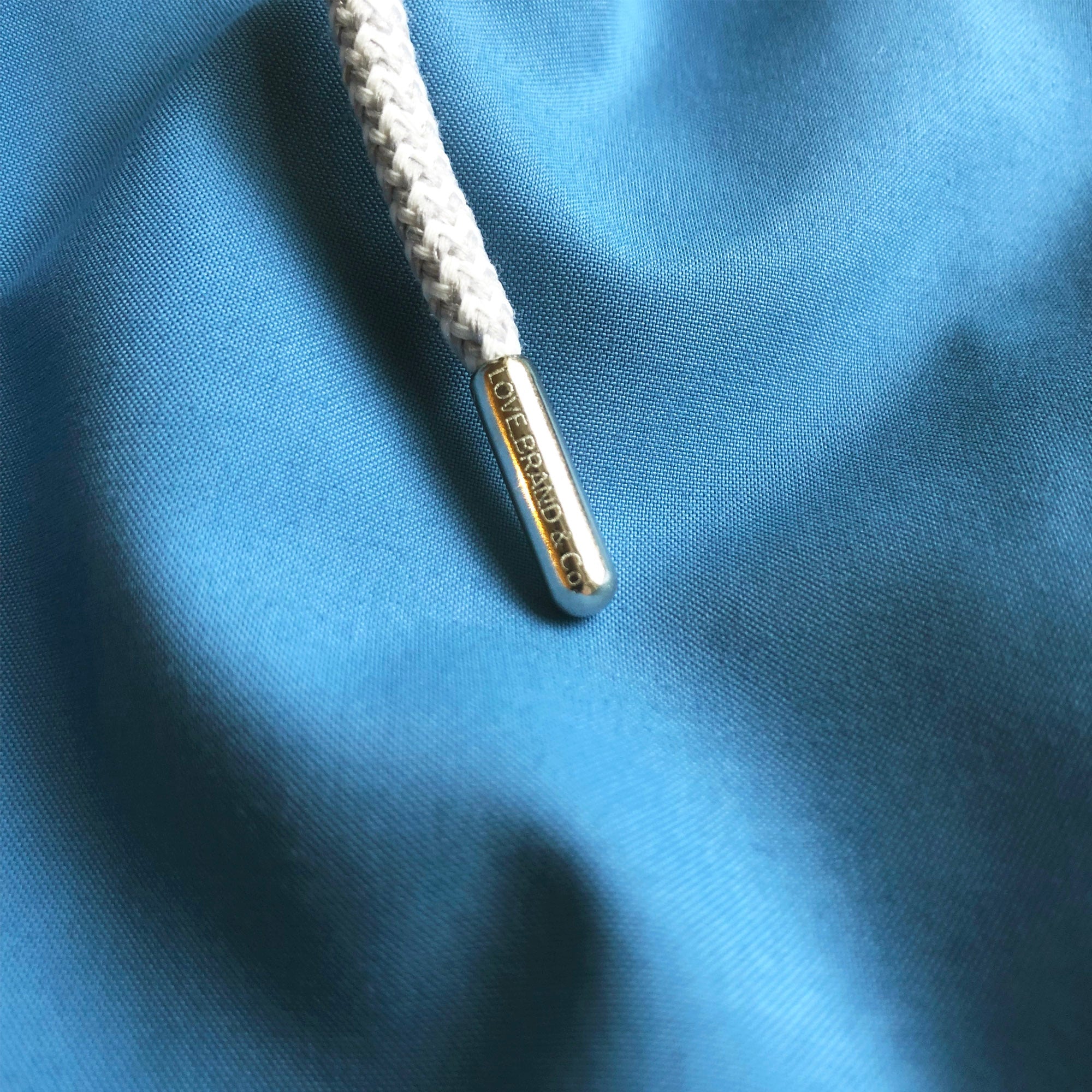 Close-up of Boys French Blue Staniel Swim Short fabric with a braided white drawstring and branded metal tip.