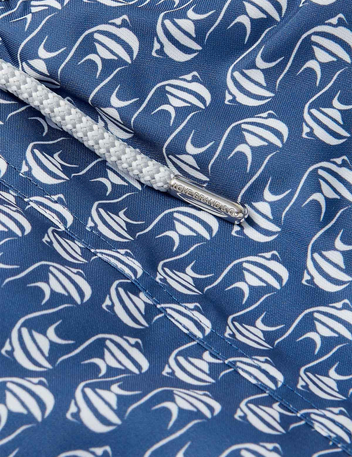 Close-up of Men's Go With the Flow Staniel Swim Shorts. Patterned swim shorts featuring a Moorish Idol fish print on a deep blue background.