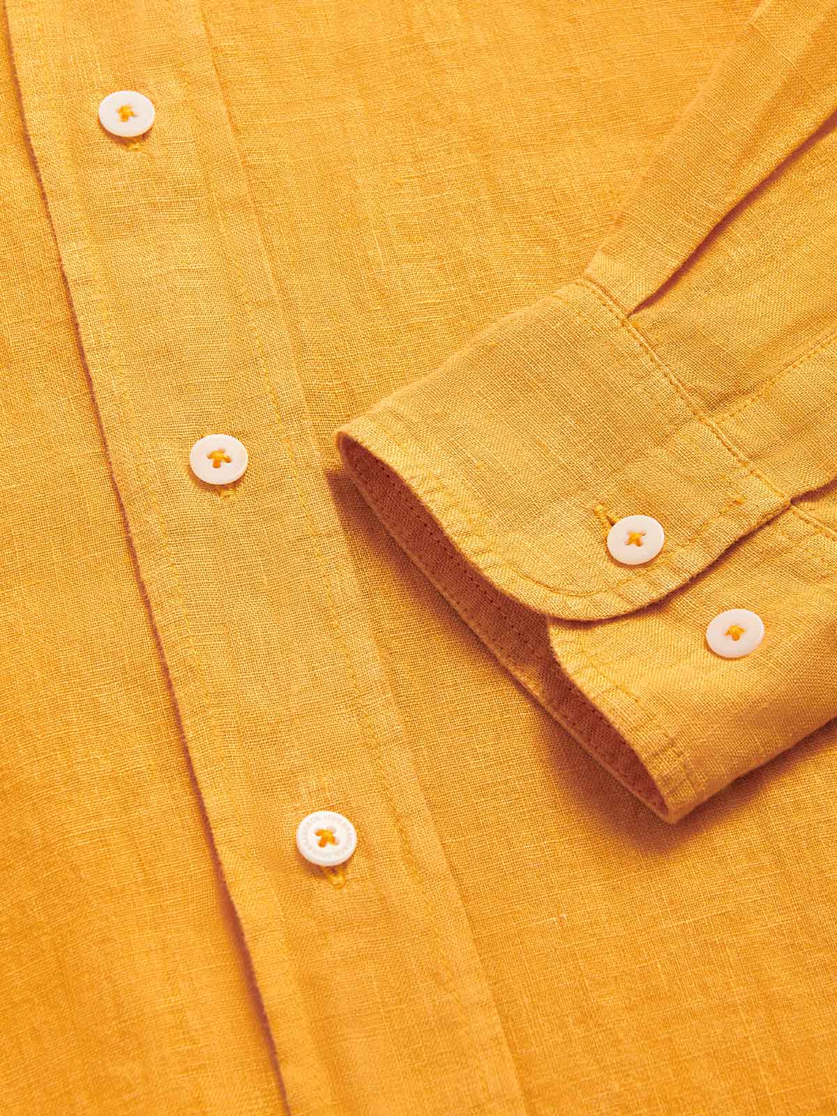 Close-up view of the Men's Golden Hour Abaco Linen Shirt showcasing the button details and linen texture in a warm golden color.