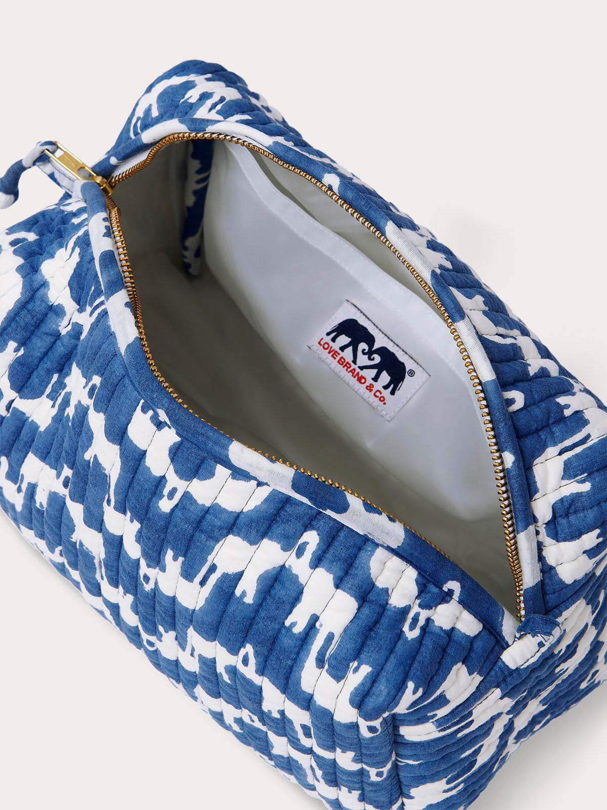 Canvas wash bag in blue featuring a block-printed pattern of Asian elephants forming the illusion of Indian palaces; shown with an open zipper displaying internal compartments and a recycled plastic lining.