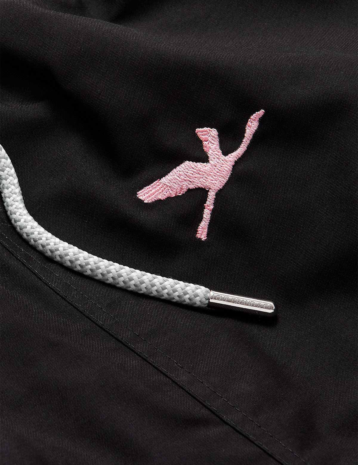 Close-up of Men's Lake Nakuru Embroidered Staniel Swim Shorts. Patterned swim shorts with pink flamingo embroidery and grey drawstring.