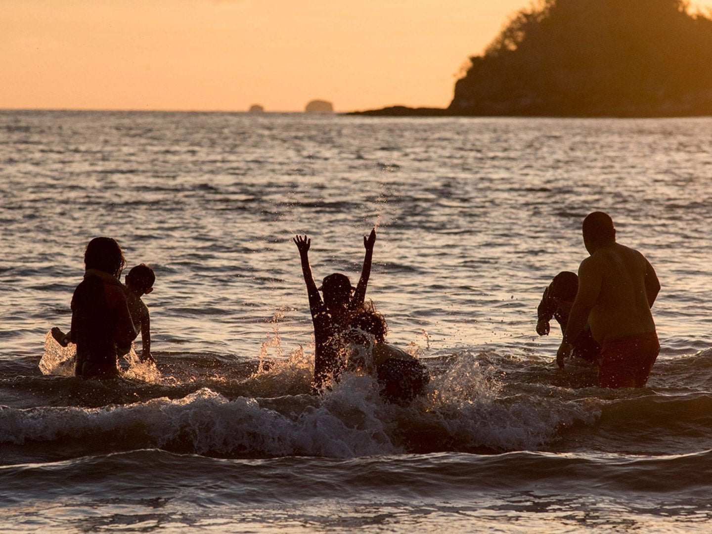 A family playing in the waters of Las Catalinas beach at sunset